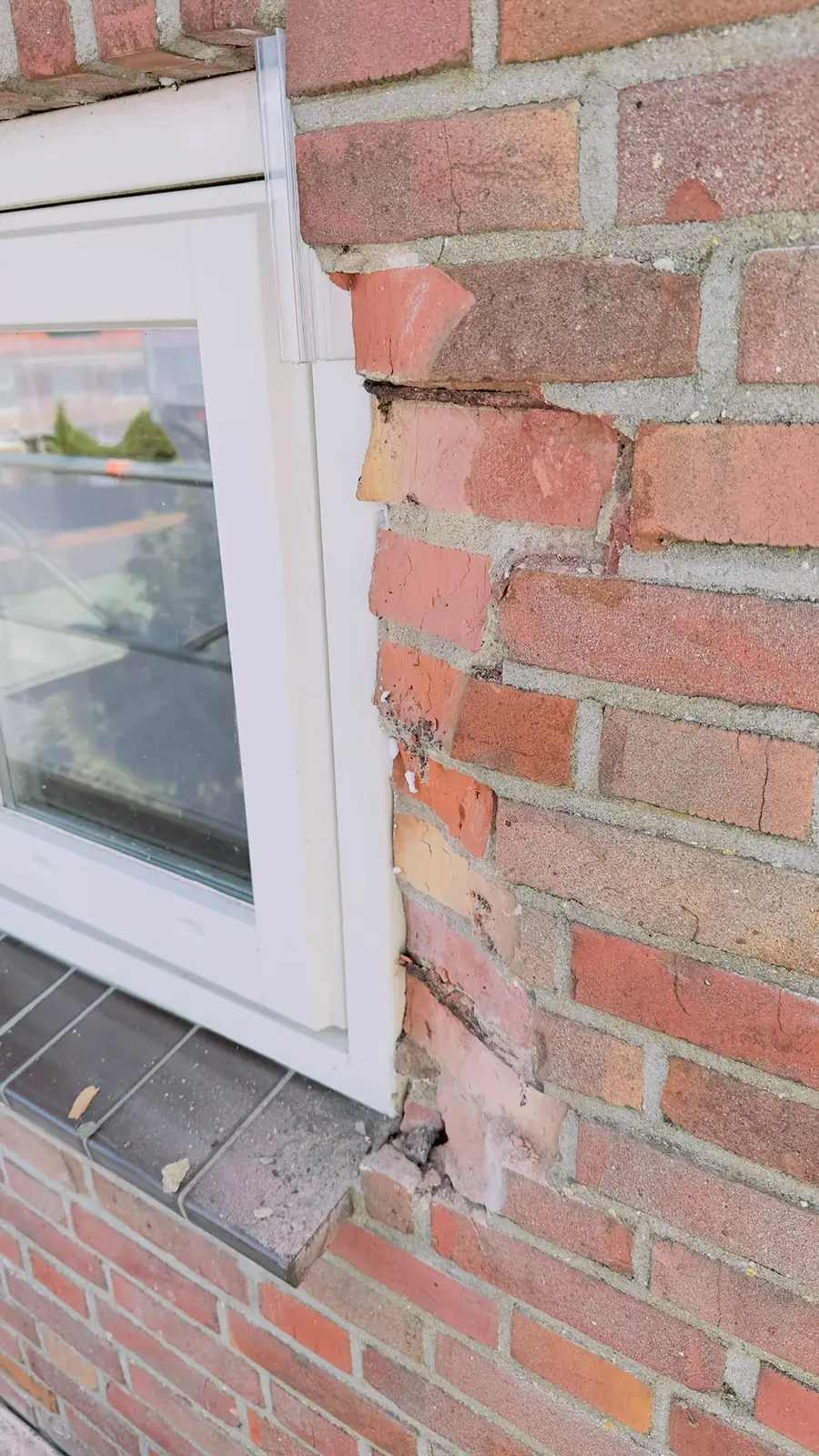 Uitgehakte voegen langs de scheur naast het raam